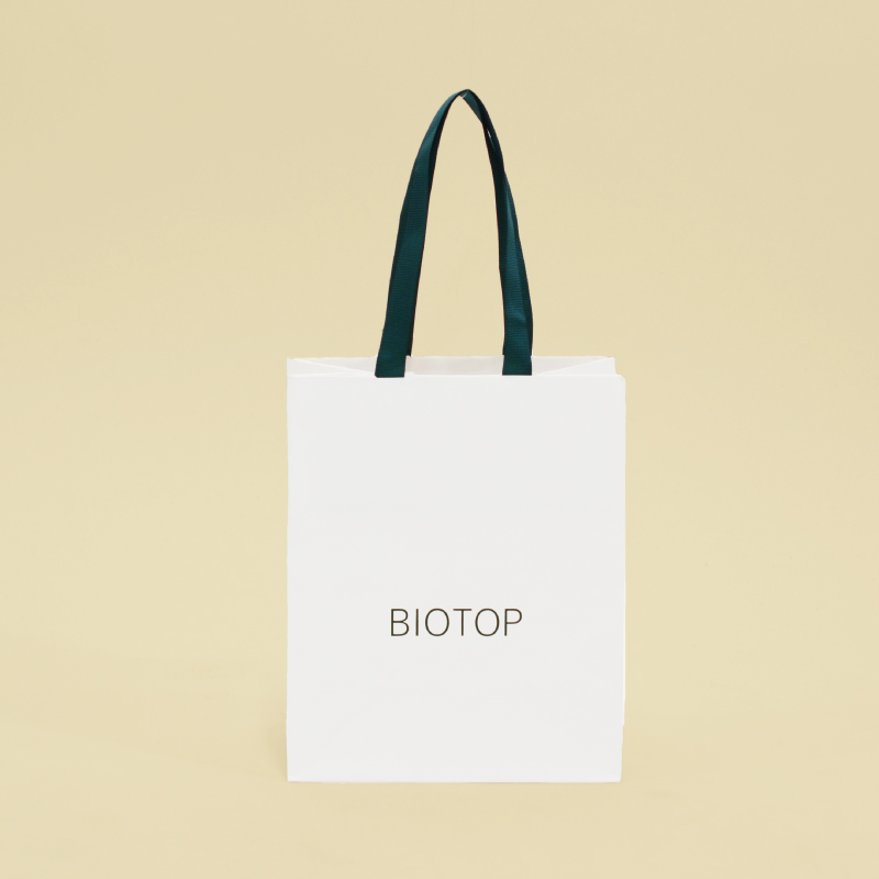 白クラフト紙に緑のリボンとロゴのナチュラルな紙袋を読む