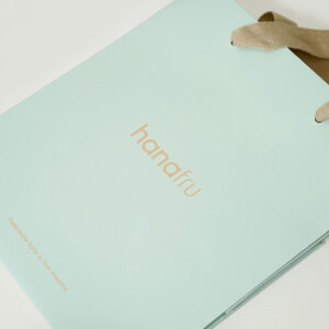 爽やかなブルーのボディに、くすみ感のあるベージュのアクリル平紐ハンドルを合わせた、フルーツ&デザートショップのオリジナル紙袋