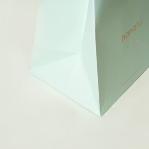 爽やかなブルーのボディに、くすみ感のあるベージュのアクリル平紐ハンドルを合わせた、フルーツ&デザートショップのオリジナル紙袋