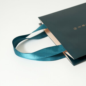 ピーコックグリーンとサテンリボンが美しい、高級感のあるコスメブランドのオリジナル紙袋
