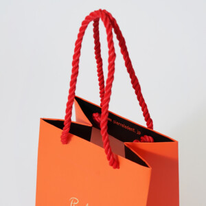 ショコラブランドの、ツイストロープがアクセントになった鮮やかなオレンジカラーのオリジナル紙袋