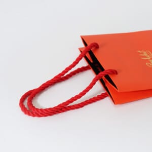 ショコラブランドの、ツイストロープがアクセントになった鮮やかなオレンジカラーのオリジナル紙袋