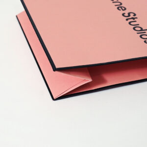 コーラルピンクを全面印刷で表現し、ロゴに箔押し加工が施した、有名ファッションブランドのリニューアルしたオリジナル紙袋