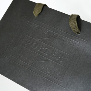 歴史ある鞄メーカーのブランドロゴにエンボス加工が施された、インパクトのあるオリジナル紙袋 