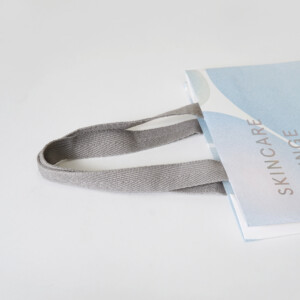 化粧品ブランドが手がけた、体験特化型施設のシェルグレー色のアクリル平紐がアクセントになったオリジナル紙袋