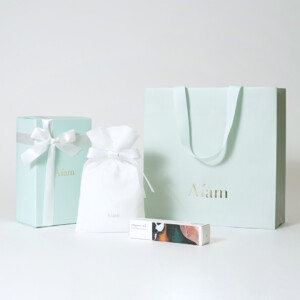 V字折り底とゴールドの箔押し加工を施した、鮮やかなミントグリーン色のフレグランスブランドのオリジナル紙袋と、ミントグリーンとホワイトでまとめられたオリジナルボックスと不織布巾着