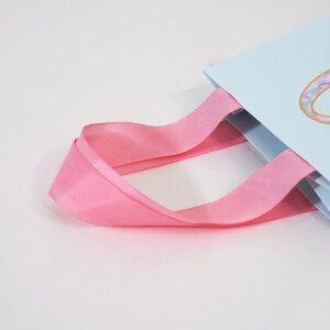 鮮やかなピンク色のグログランリボンのハンドルが目を惹く、高級コスメブランドのオリジナル紙袋