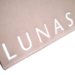 くすみ感のあるベージュカラーのボディにエンボス加工と箔押しが施された、高級コスメブランドのエレガントなオリジナル紙袋