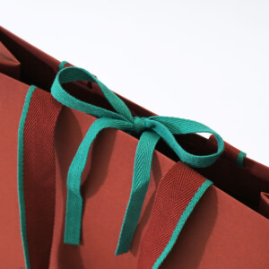 グリーンとブラウンの2色使いが印象的なアクリル平紐を使用した、深い歴史のある服地のトップメーカーの高級感溢れるオリジナル紙袋