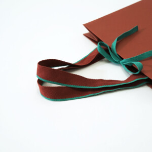 グリーンとブラウンの2色使いが印象的なアクリル平紐を使用した、深い歴史のある服地のトップメーカーの高級感溢れるオリジナル紙袋