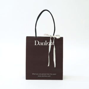 温かみのあるこげ茶色に黒い紐と白い差し色という配色に、「エンボス加工」「縦留め」「リボン印刷」などの加工が調和した、東京発のフレグランスブランドのオリジナル紙袋