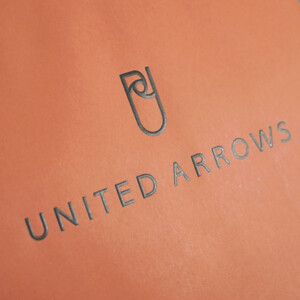 落ち着いたオレンジ色にブラックの箔押しのブランドロゴが映える、大人に向けたドレス軸のライフスタイルを提案するセレクトショップのオリジナル紙袋