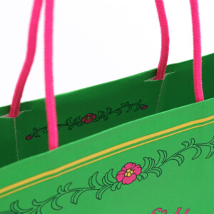 ポップなカラーのハンドルがかわいい、フルカラー印刷でレトロな花と可愛らしい帽子が表現された、ジブリパークのグッズショップ「ハッター帽子店」のオリジナル紙袋 